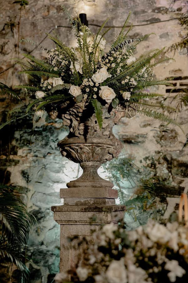 Arreglo floral alto de rosas blancas y helecho sobre pedestal de piedra