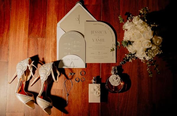 Invitación de boda con zapatos, argollas y perfume dispuestos sobre madera
