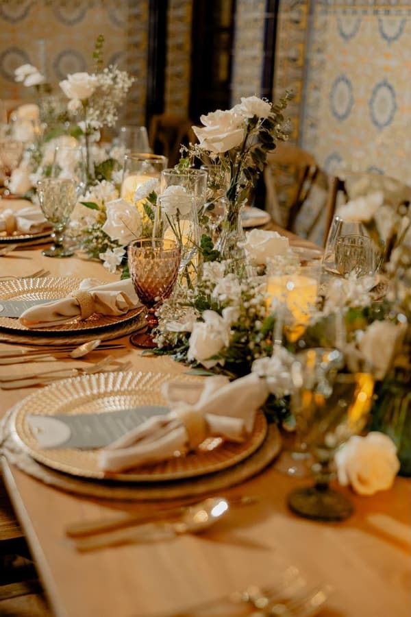 Mesa imperial de boda con camino de rosas blancas, copas y platos de ratán