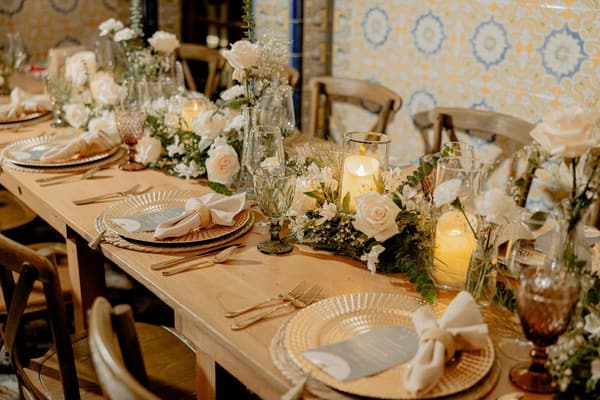 Mesa larga de banquete con centro de flores blancas, velas y sillas de madera