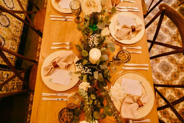 Mesa de madera con camino de eucalipto, velas y platos de ratán
