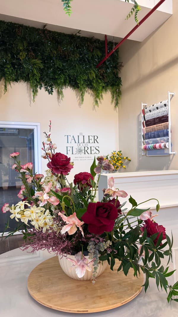 Arreglo de rosas y peonías vino recién terminado en el mostrador del taller, frente al muro con el logo de El Taller de las Flores